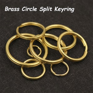 May include: A set of gold-coloured brass split keyrings of various sizes. The keyrings are made of metal and have a circular shape.