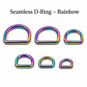 Può includere: Sei anelli a D senza saldatura disposti su due file, caratterizzati da una finitura metallica arcobaleno con sfumature iridescenti di blu, viola, verde e giallo. Il testo Seamless D-Ring -- Rainbow è visualizzato sopra i componenti.