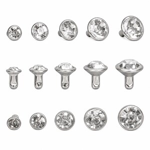 May include: A collection of clear, faceted crystal jewelry pieces with a silver-colored metal base. The pieces vary in size and shape, including flat-backed studs and post-style settings. The crystals sparkle, reflecting light.
