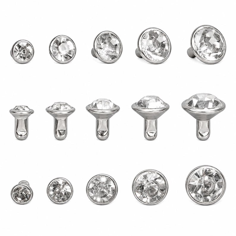 May include: A collection of clear, faceted crystal jewelry pieces with a silver-colored metal base. The pieces vary in size and shape, including flat-backed studs and post-style settings. The crystals sparkle, reflecting light.