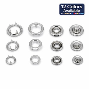 Puede incluir: Una colección de broches de presión plateados, exhibidos sobre un fondo blanco. La imagen muestra varios tamaños y estilos de broches, incluyendo diseños en forma de anillo y de botón. Un banner en la esquina superior derecha indica que hay 12 colores disponibles.