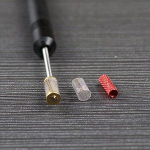 Peut inclure: Un outil noir avec une pointe m&eacute;tallique et trois embouts m&eacute;talliques de diff&eacute;rentes tailles. Les embouts sont un cylindre en maille argent&eacute;e, un cylindre en maille argent&eacute;e et un cylindre rouge.