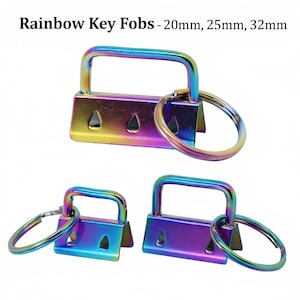 May include: Rainbow key fobs in iridescent colors with key rings. The key fobs are rectangular with a curved handle and three triangular cutouts. The text "Rainbow Key Fobs - 20mm, 25mm, 32mm" is at the top.