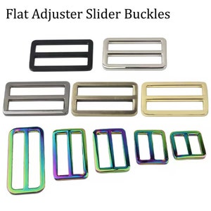 May include: Assortment of flat adjuster slider buckles in various finishes, including black, silver, gold, and iridescent rainbow. The buckles are rectangular with two parallel bars.