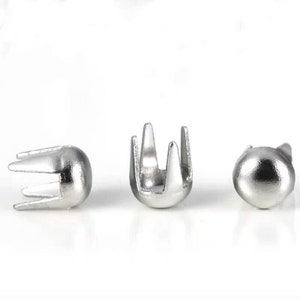 May include: Three silver metal rivets with a pointed tip and a decorative crown-like top. The rivets are used for attaching fabric or leather.