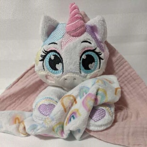 May include: A white unicorn plush toy with rainbow and heart embroidery, holding a pink and white blanket with rainbow and heart patterns.