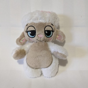 以下が含まれることがあります： ピンクの鼻と青い目をした白いぬいぐるみの子羊。子羊は白いふわふわの頭とベージュの体をしている。