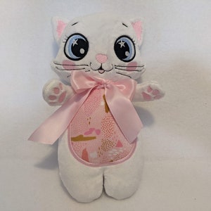 May include: White plush cat toy with pink bow and a pink and gold patterned fabric on the chest. The cat has embroidered blue eyes and a pink nose.