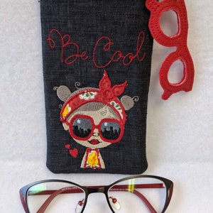 May include: A black eyeglass case with the embroidered phrase "Be Cool" in red, featuring a cartoon girl with sunglasses. A red glasses-shaped keychain hangs from the zipper. Below, a pair of black and red eyeglasses.
