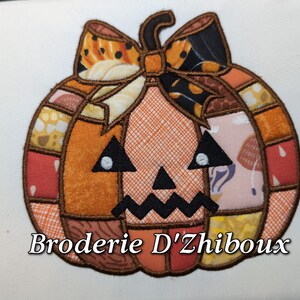 Op de afbeelding: Geborduurde pompoen applicatie met een patchwork ontwerp. De pompoen heeft een steel en strik, met een jack-o'-lantern gezicht. De tekst "Broderie D'Zhiboux" staat onderaan. Het ontwerp bevat oranje, bruin, zwart en diverse stoffen met patronen.