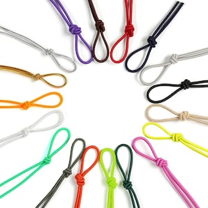 Könnte beinhalten: Sortiment von 18 bunten Gummibändern, jedes zu einer Schlaufe gebunden mit einem Knoten oben. Die Bänder sind in einem Kreis auf weißem Hintergrund angeordnet.