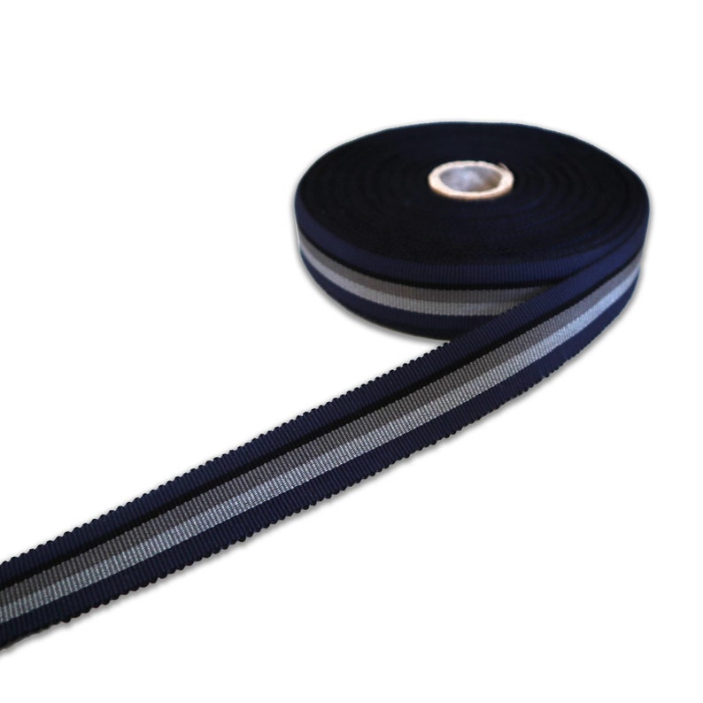 May include: A roll of navy blue ribbon with two silver stripes. The ribbon is approximately 2.5 cm wide.