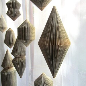 May include: A collection of geometric paper ornaments made from the pages of old books. The ornaments are suspended from the ceiling and are made in a variety of shapes, including diamonds, triangles, and squares.