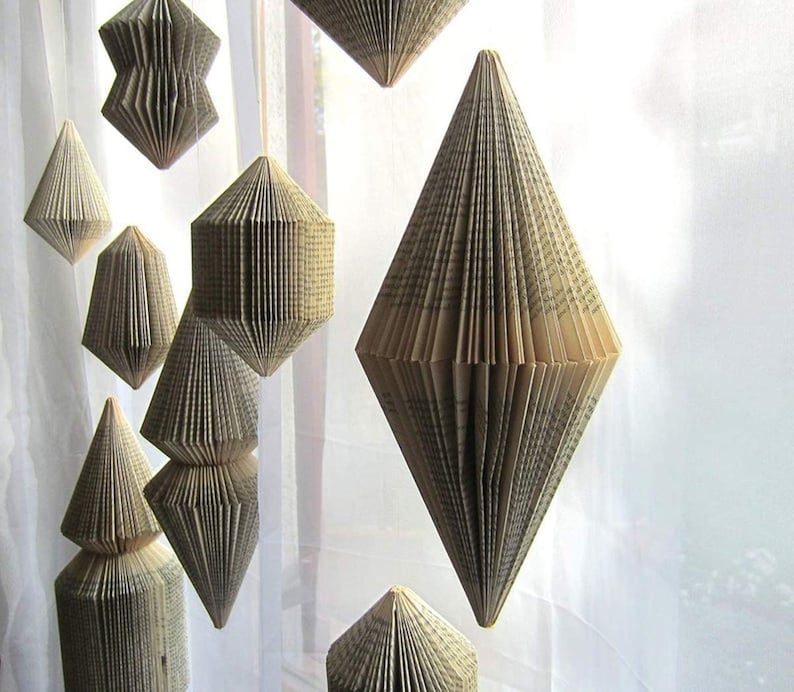 May include: A collection of geometric paper ornaments made from the pages of old books. The ornaments are suspended from the ceiling and are made in a variety of shapes, including diamonds, triangles, and squares.