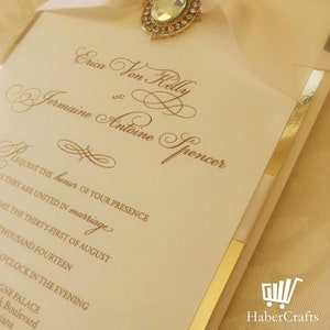 K&ouml;nnte beinhalten: Eine Hochzeitseinladung mit goldenen Akzenten und cremefarbenem Hintergrund. Die Einladung lautet "Erica Von Kelly und Jermaine Antoine Spencer bitten um die Ehre Ihrer Anwesenheit bei ihrer Hochzeit Am dreiunddrei&szlig;igsten August Zweitausendvierzehn Um achtzehn Uhr Das Grand Palace Boulevard Indiana"