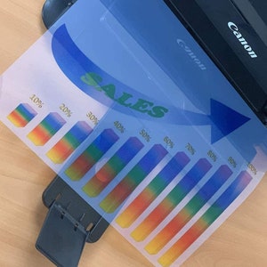 May include: A sales chart with a rainbow gradient bar graph showing percentages from 10% to 100%. The chart is printed on a clear plastic sheet and is being fed into a Canon scanner.