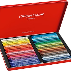 Peut inclure: Une boîte métallique rouge ouverte contenant des crayons Caran d'Ache Neocolor II. Le couvercle porte le logo Caran d'Ache et le mot "Genève". Les crayons, de couleurs variées, sont rangés en deux sections, offrant une large gamme de nuances.