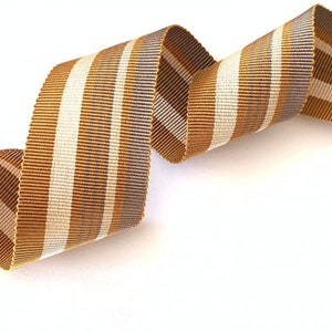 May include: A brown and white striped ribbon with a subtle shimmer. The ribbon is curled and twisted, showing off its texture.