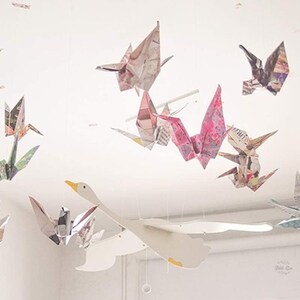 May include: A white paper swan mobile with colorful paper origami birds hanging from it. The mobile is made of paper and is a great addition to any nursery or child's room.