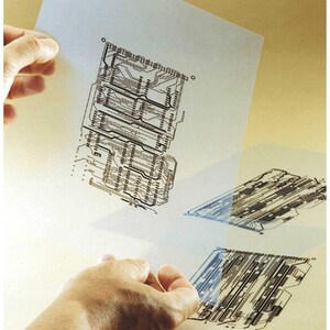 May include: A close-up of a person holding a transparent sheet with a black and white circuit board design printed on it. The sheet is slightly translucent, allowing the design to be seen through it.