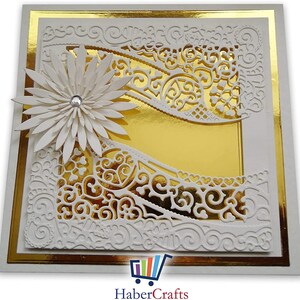 K&ouml;nnte beinhalten: Eine wei&szlig;e Karte mit goldfarbenem Rand und einem wei&szlig;en Papier-Serviettenmuster. Das Serviettenmuster hat eine wei&szlig;e Blume mit einem Strassstein in der Mitte oben links. Die Karte ist leer und bereit f&uuml;r eine Nachricht.