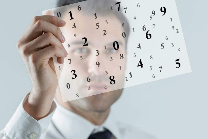 May include: A person holds a sheet of paper with a grid of numbers printed on it. The numbers are arranged in a random pattern. The person's face is blurred in the background.