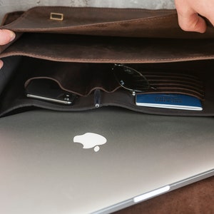 May include: A brown leather messenger bag with a laptop, sunglasses, and a passport inside. The bag has a flap closure and a buckle.