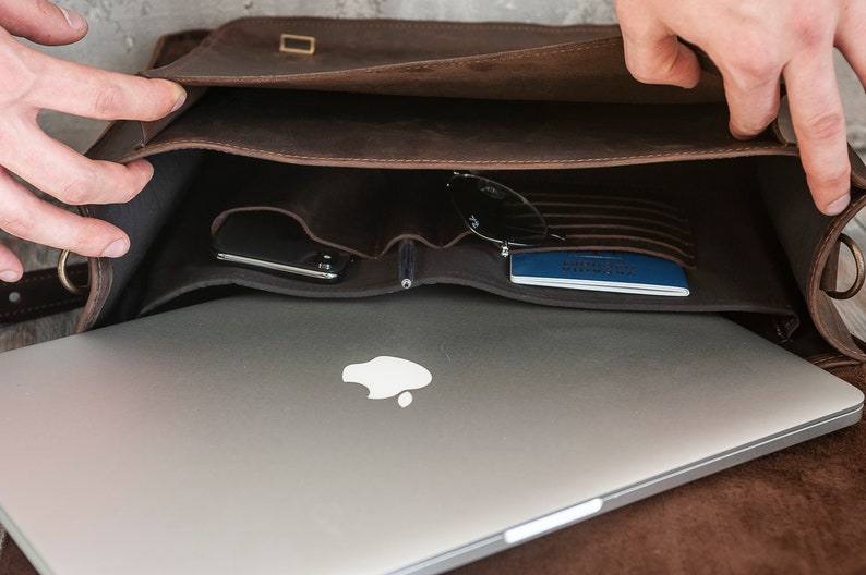 May include: A brown leather messenger bag with a laptop, sunglasses, and a passport inside. The bag has a flap closure and a buckle.