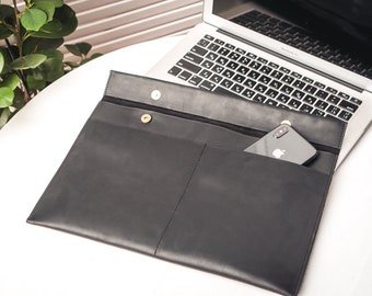 Könnte beinhalten: Eine schwarze Lederhülle für Laptops mit einem Fach für ein Telefon. Die Hülle ist geöffnet und ein Laptop und ein Telefon befinden sich darin.