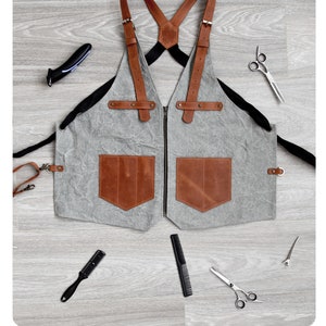 May include: A gray canvas and brown leather apron with adjustable straps and two large pockets. The apron measures 51 inches in height and 25 inches in width.