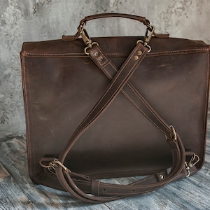 May include: A brown leather briefcase with adjustable straps. The briefcase has a top handle and a flap closure.
