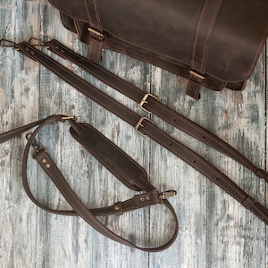 May include: Three brown leather straps with brass buckles and clasps. The straps are for a bag or backpack.