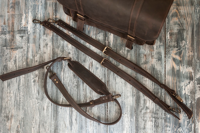 May include: Three brown leather straps with brass buckles and clasps. The straps are for a bag or backpack.