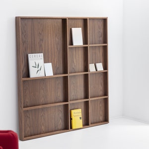 May include: A brown wooden bookshelf with nine shelves, each divided into two sections. The shelves are filled with books and magazines, including one with the word "Cereal" on the cover.