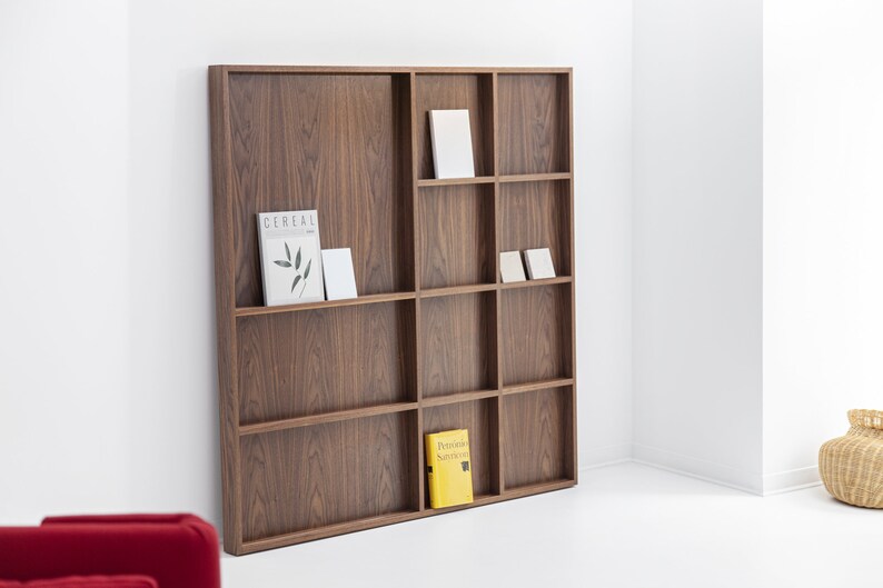 May include: A brown wooden bookshelf with nine shelves, each divided into two sections. The shelves are filled with books and magazines, including one with the word "Cereal" on the cover.