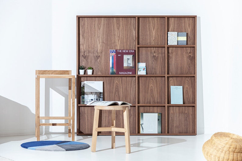 May include: A wooden bookshelf with nine shelves, featuring a variety of books and magazines. The bookshelf is made of dark wood and has a simple, modern design. The bookshelf is in a room with a white wall and a light wood floor.