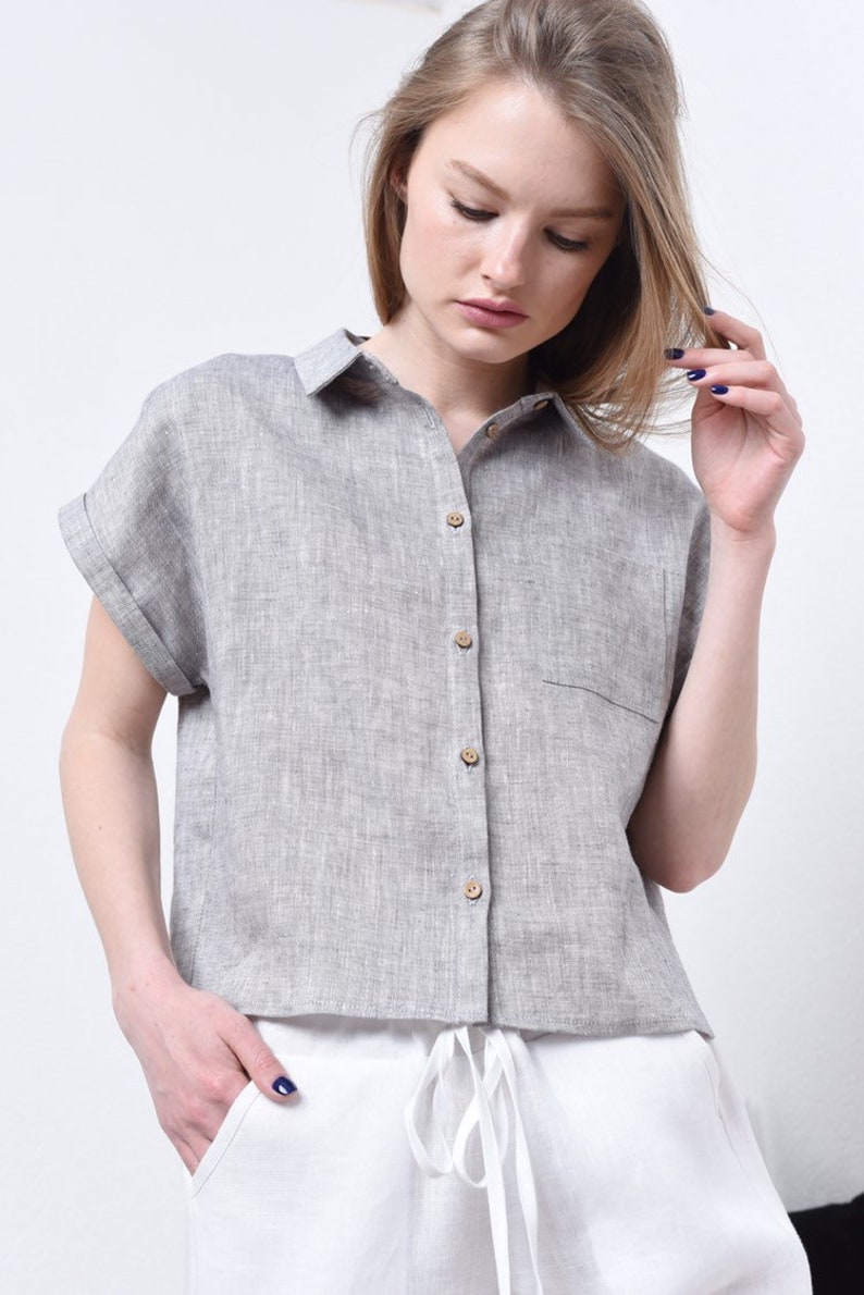May include: A gray linen shirt with short sleeves and a button-up front. The shirt has a relaxed fit and a cropped hem.