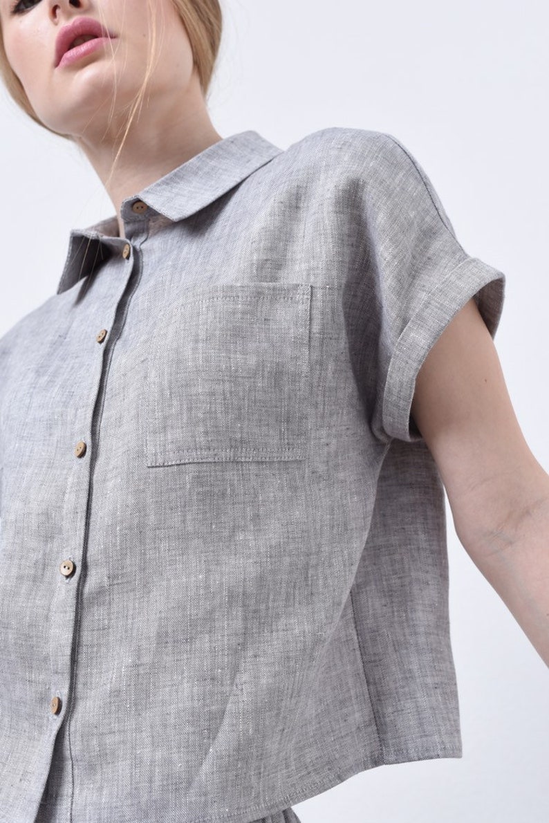May include: A gray linen shirt with a button-up front and a single chest pocket. The shirt has short sleeves with rolled cuffs.