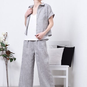 May include: A woman wearing a gray linen shirt and matching wide-leg pants. The shirt has a collar and short sleeves. The pants have a relaxed fit and are cropped at the ankle.