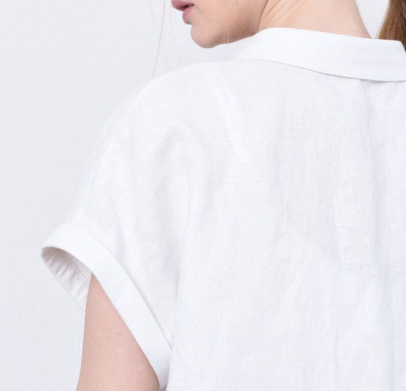 May include: White linen shirt with a collared neckline and short sleeves. The shirt has a relaxed fit and a casual style.
