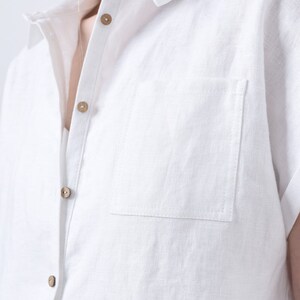 May include: A white linen shirt with a button-up front and a single chest pocket. The shirt has a classic collar and short sleeves.