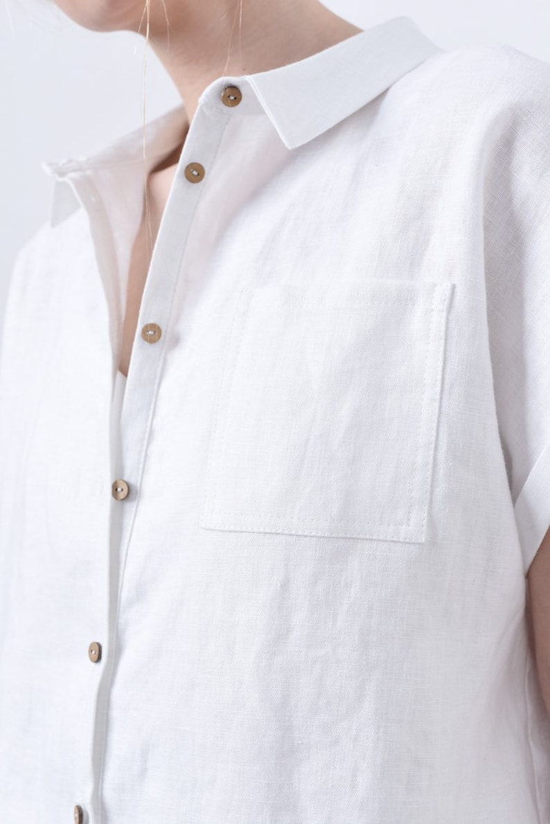 May include: A white linen shirt with a button-up front and a single chest pocket. The shirt has a classic collar and short sleeves.