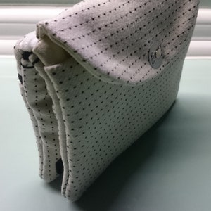 Könnte beinhalten: Eine weiße Stofftasche mit schwarzen Punkten und einem silbernen Druckknopfverschluss.