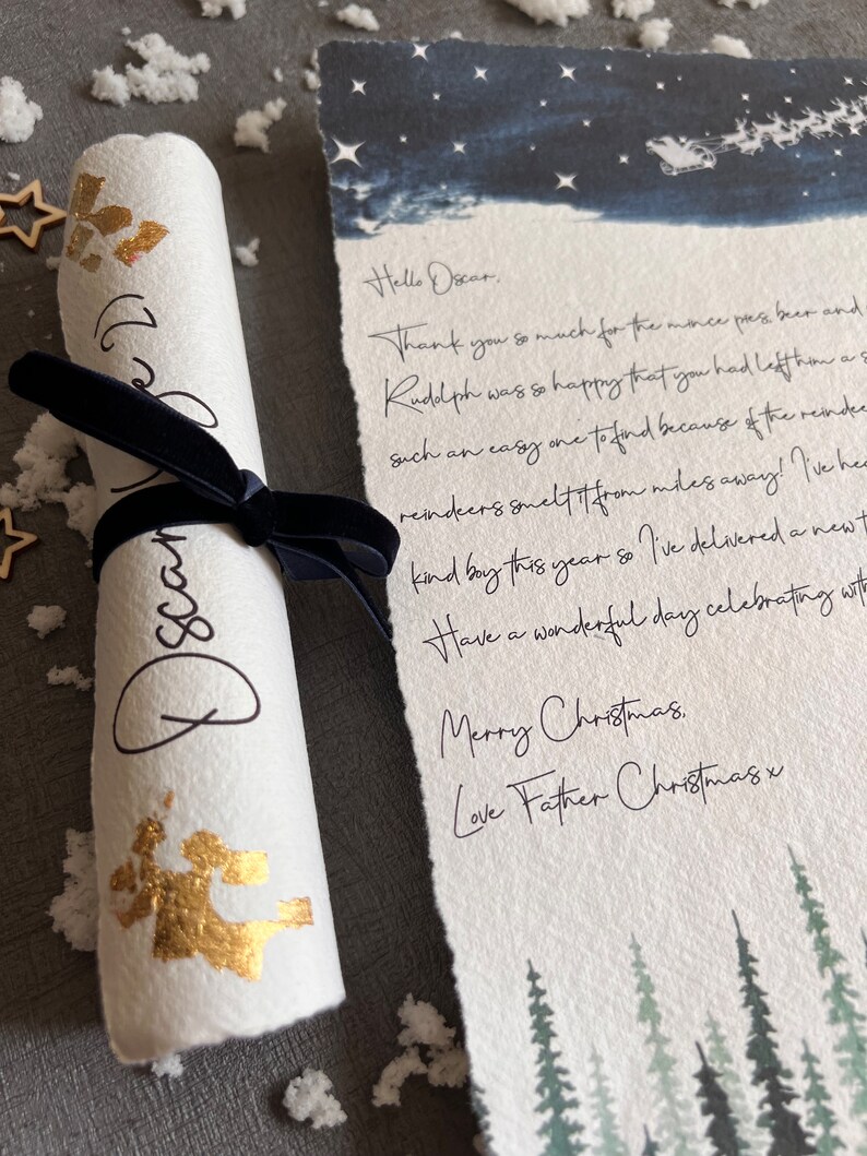 May include: A rolled up letter with gold glitter and a handwritten message that says "Hello Oscar. Thank you so much for the mince pies, beer and Rudolph was so happy that you had left him a such an easy one to find because of the reindeer. Reindeer smelt it from miles away! I've heard kind boy this year so I've delivered a newt. Have a wonderful day celebrating with Merry Christmas. Love Father Christmas x". The letter is on a white background with a blue watercolour background with stars and a silhouette of Santa's sleigh.