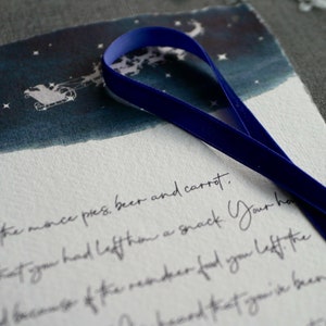 May include: A handwritten note with blue ribbon on top. The note says "ch for the monce pres, beer and carrot. -ppy that you had left han a snack Your ha and because of the reindeer food you left the"
