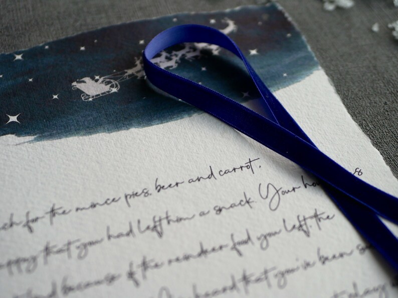 May include: A handwritten note with blue ribbon on top. The note says "ch for the monce pres, beer and carrot. -ppy that you had left han a snack Your ha and because of the reindeer food you left the"