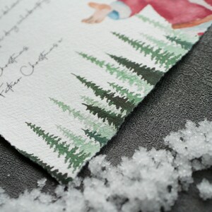 May include: A watercolour Christmas card with a handwritten message that reads "Merry Christmas Love Father Christmas". The card features a snowy forest scene with green pine trees.