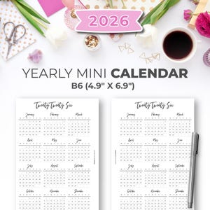 Może przedstawiać: Roczny mini kalendarz na rok 2026, format B6 (12,4 cm x 17,5 cm). Kalendarz jest czarno-biały o prostym designie. Obraz zawiera długopis, filiżankę kawy, kwiaty i artykuły papiernicze.