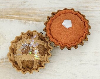May include: Two felt pie decorations, one with a brown crust and a sparkly filling, the other with an orange crust and a white dollop of filling.