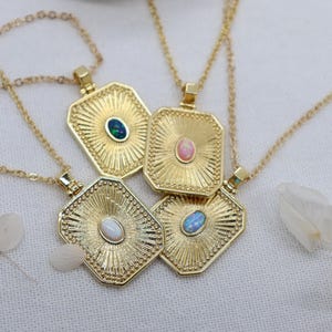 May include: Four gold necklaces with rectangular pendants. Each pendant features a central gemstone in green, pink, white, and blue. The pendants have a sunburst design and are on delicate gold chains.